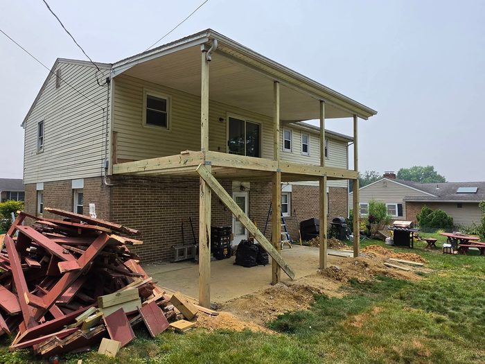 New pressure-treated posts and beam carrying the porch roof, with the demolished deck stacked nearby — Central Pennsylvania